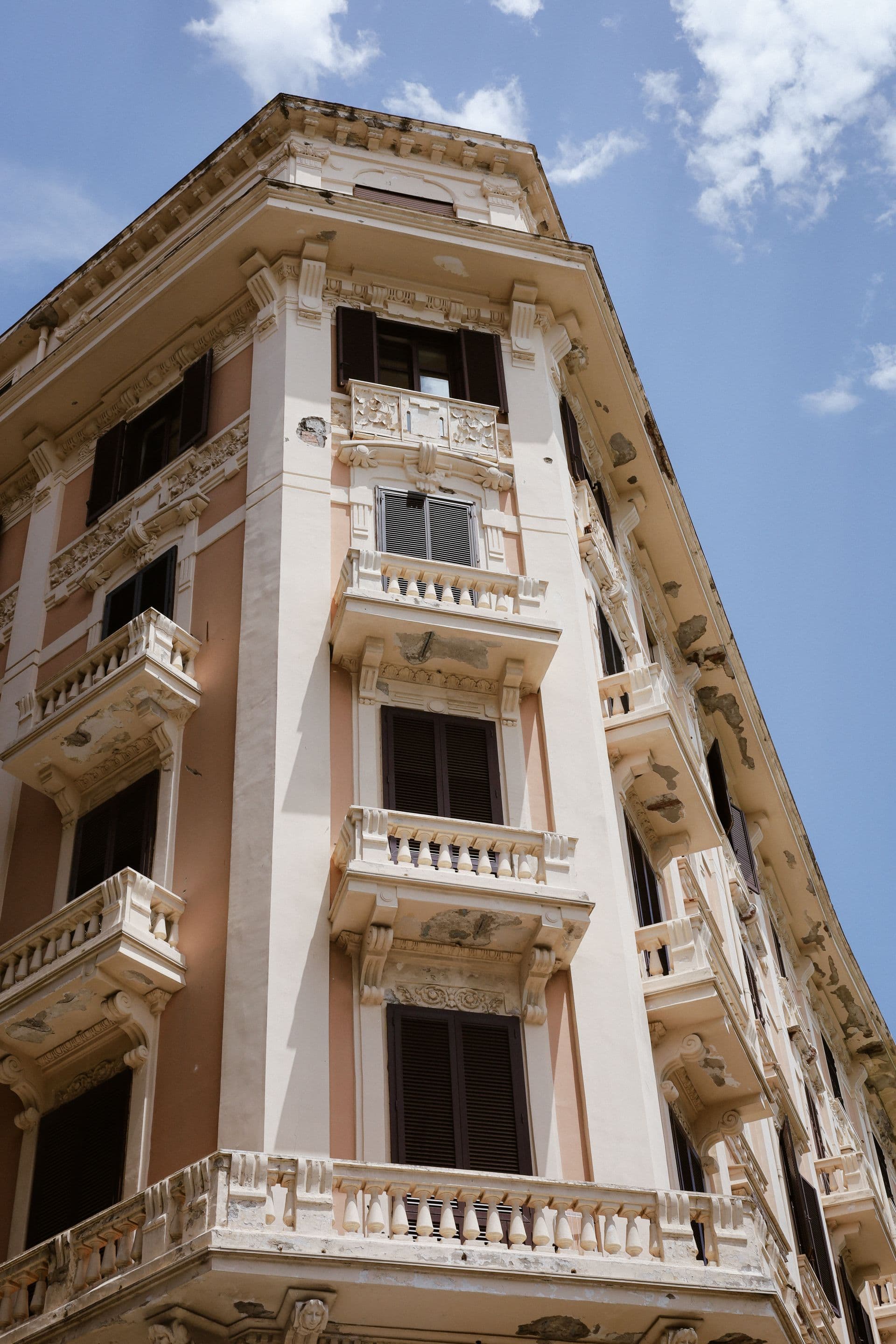 Façade d'un immeuble résidentiel de style haussmannien sous un soleil estival intense, illustrant le bâti ancien exposé à la surchauffe et la nécessité d'adapter le parc français aux vagues de chaleur