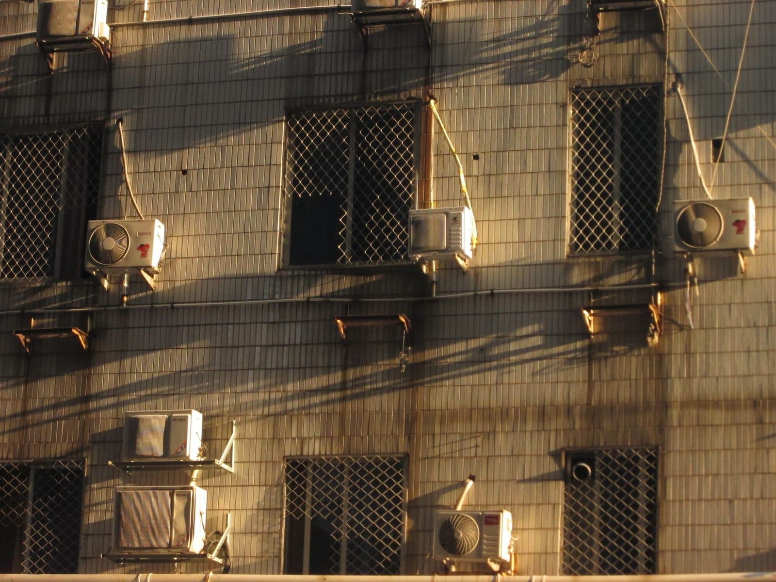 Unità esterne di condizionatori fissate sulla facciata di un edificio con finestre dotate di grate