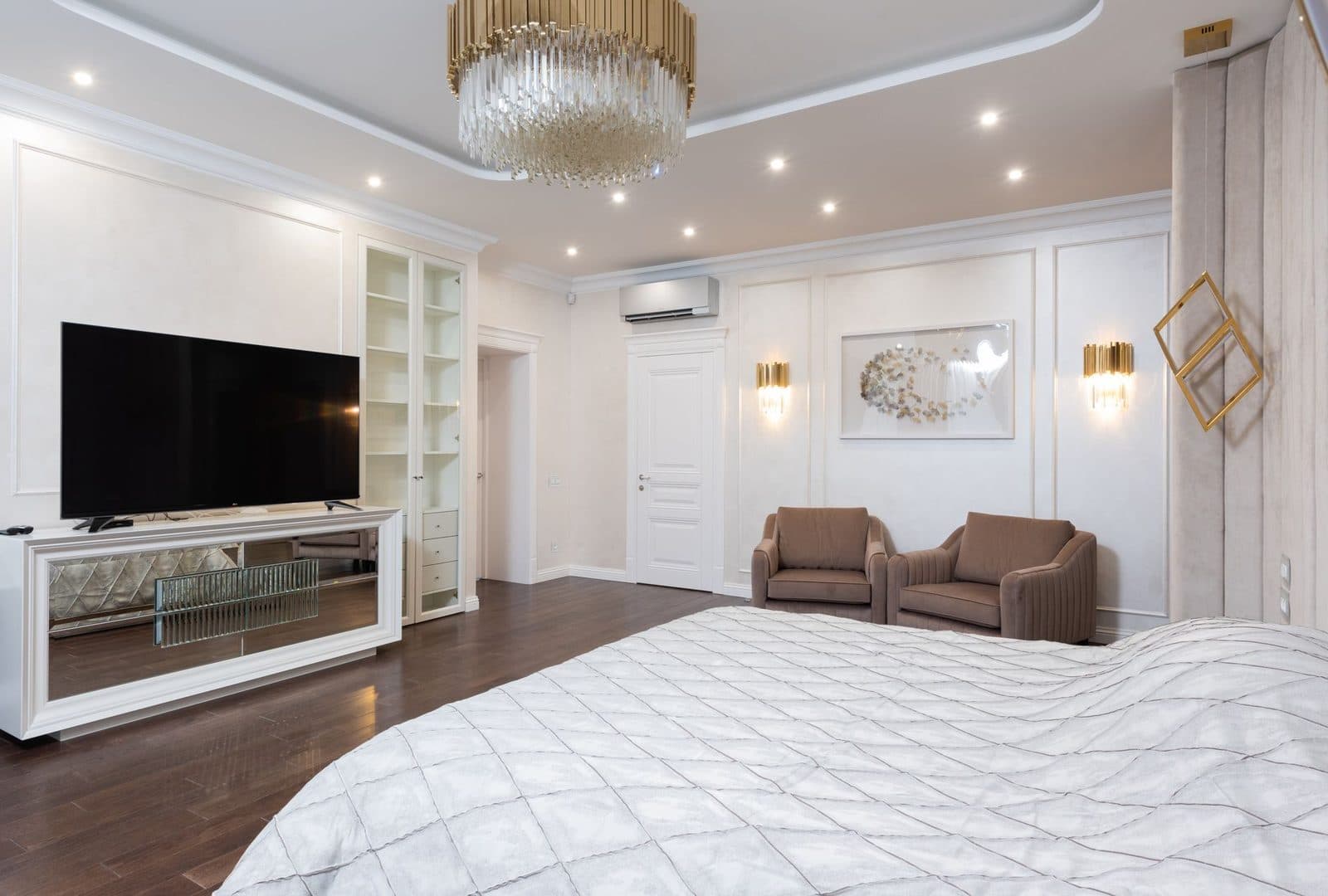 Wandunit van een reversibele airconditioning in een ruime slaapkamer met bed en fauteuils