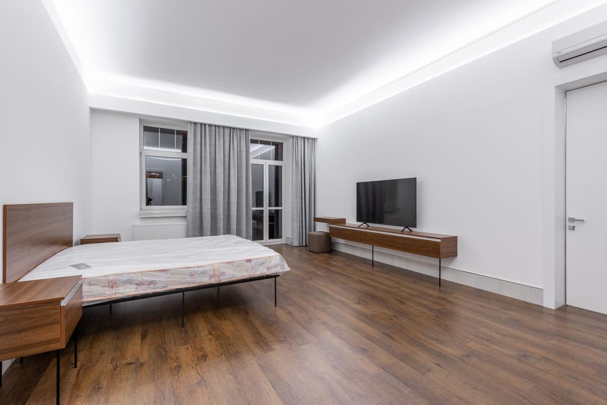 Helles Schlafzimmer mit Parkettboden, Bett, Fernseher und Wandgerät einer reversiblen Klimaanlage nahe der Decke