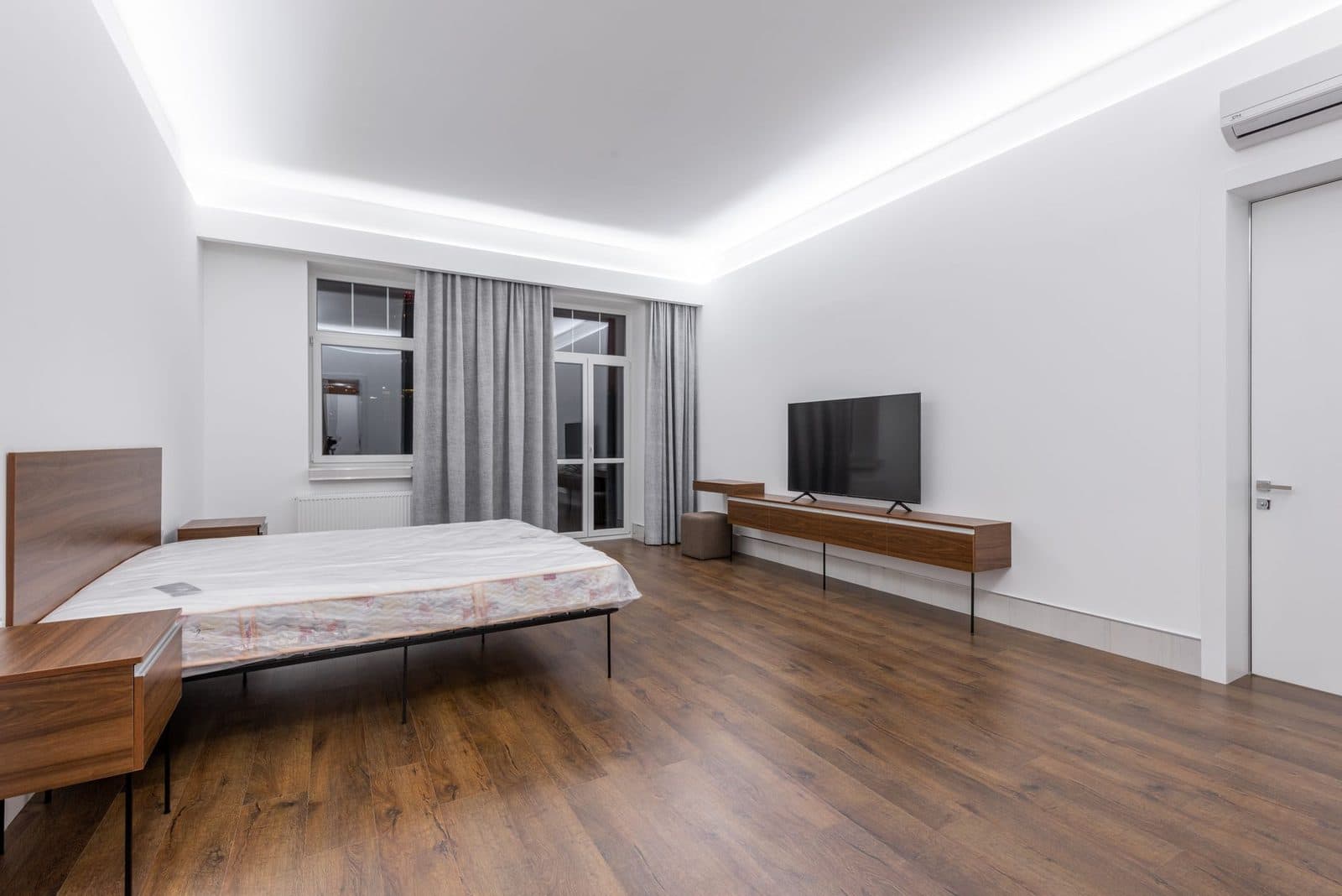 Camera luminosa con parquet, letto, televisore e unità a parete di climatizzazione reversibile vicino al soffitto