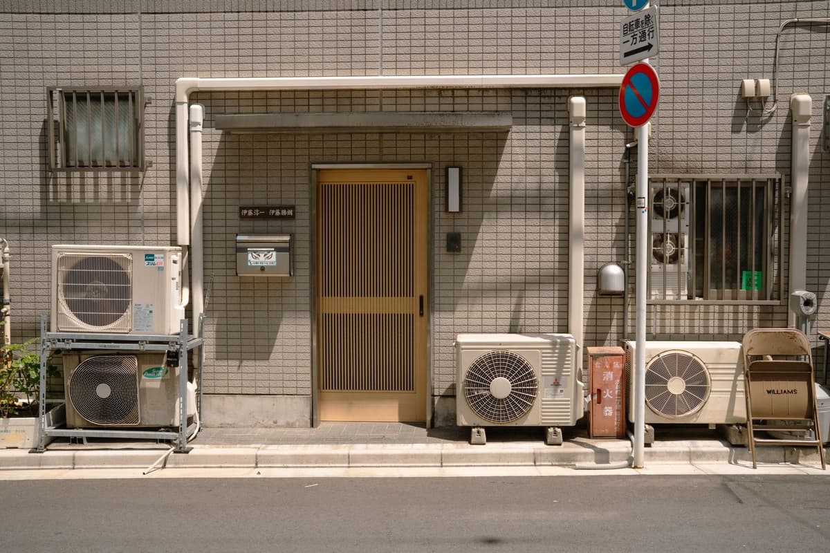 Unités extérieures de climatiseurs alignées devant la façade carrelée d'une maison, près de la porte d'entrée