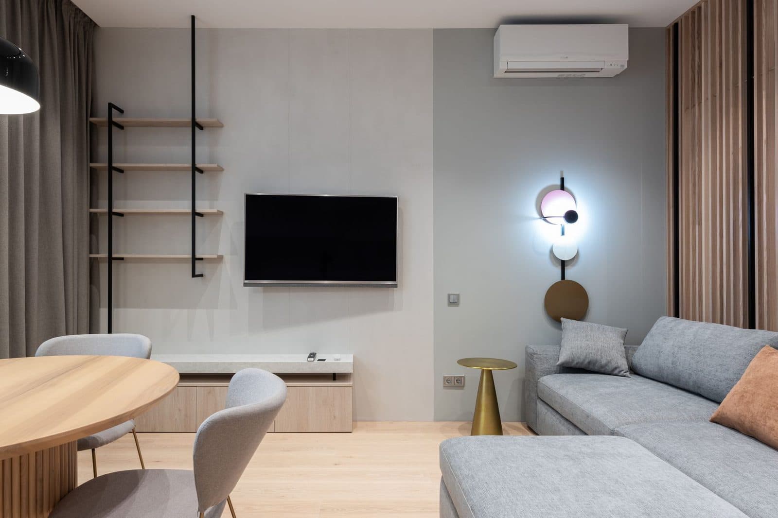 Aire acondicionado de pared blanco instalado en alto en un salón moderno con sofá gris y televisión