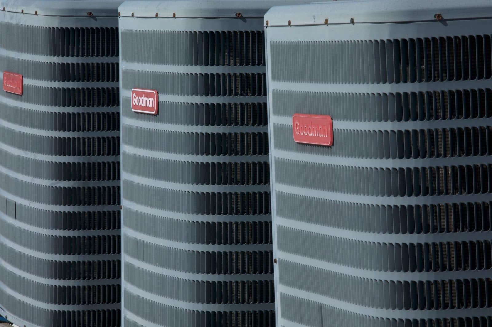 Drie buitenunits van airconditioning op een rij, grijze metalen roosters en rode merkplaatjes