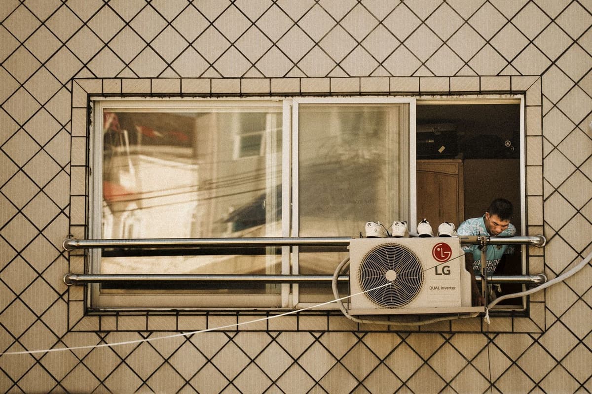 Außengerät einer Klimaanlage unter einem Fenster montiert, darüber ein Mann, der sich aus dem Fenster lehnt