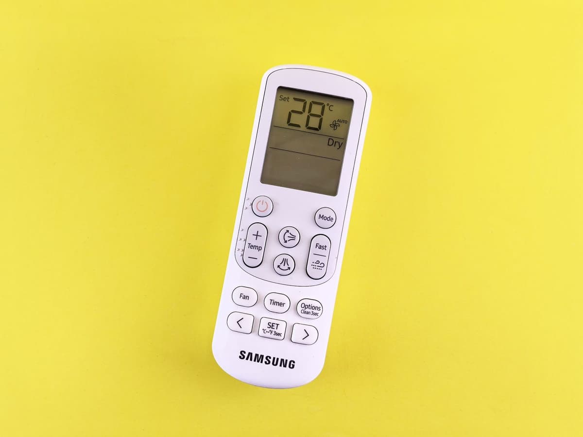 Mando a distancia blanco de aire acondicionado que muestra 28 °C en modo Dry, sobre fondo amarillo