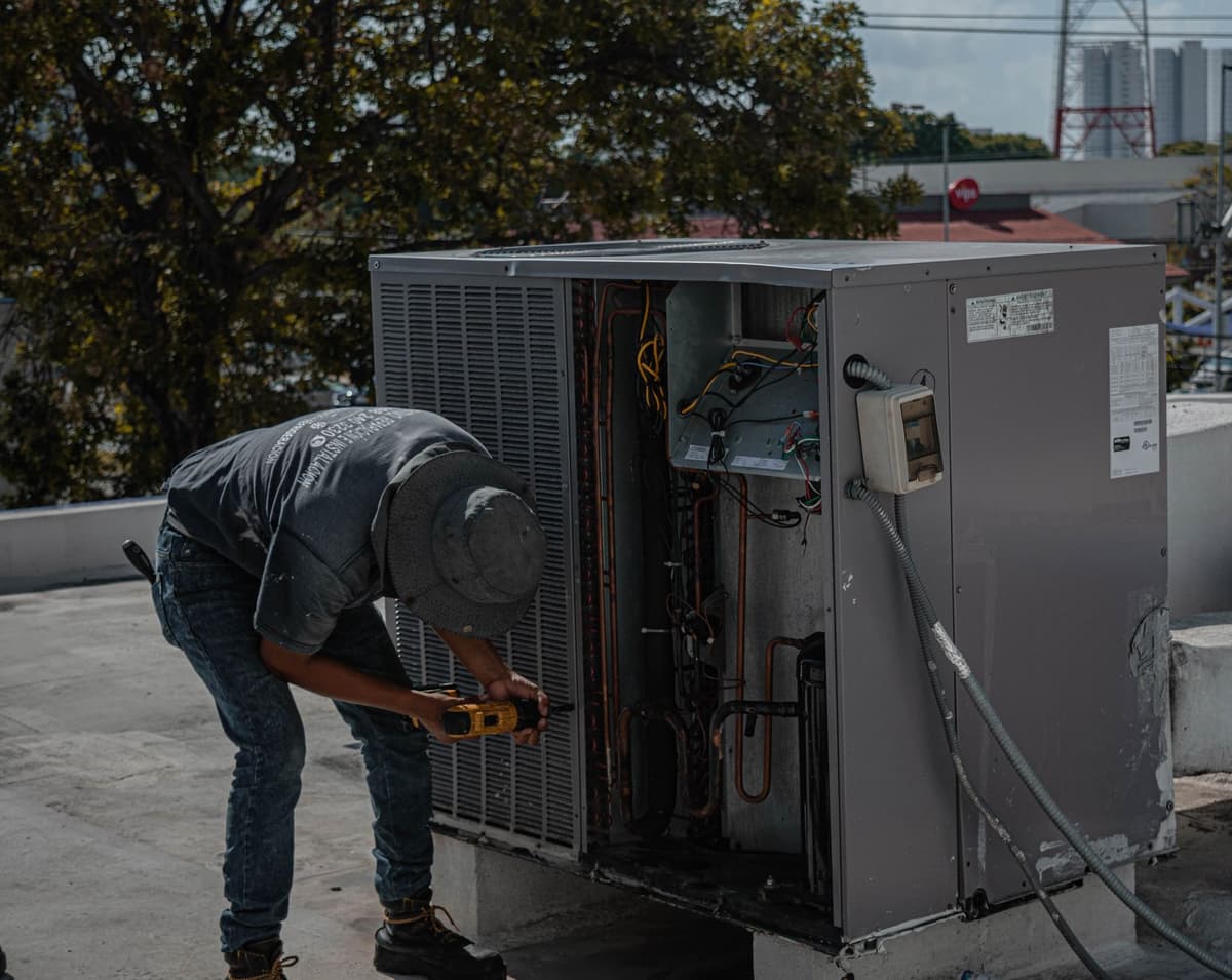 Un technicien utilisant une perceuse pour réparer une unité extérieure de climatisation sur un toit.