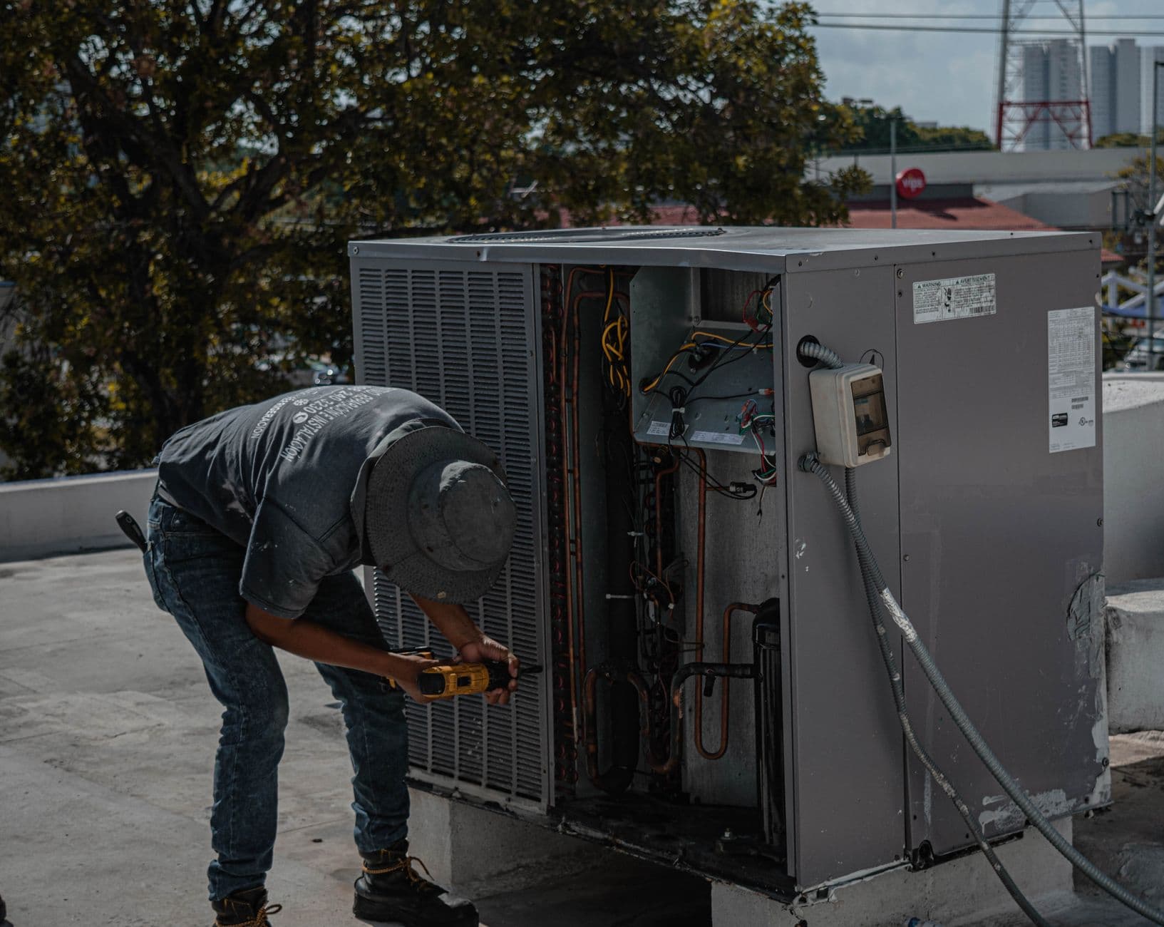 Un tecnico che utilizza un trapano per riparare un'unità esterna di climatizzazione su un tetto.