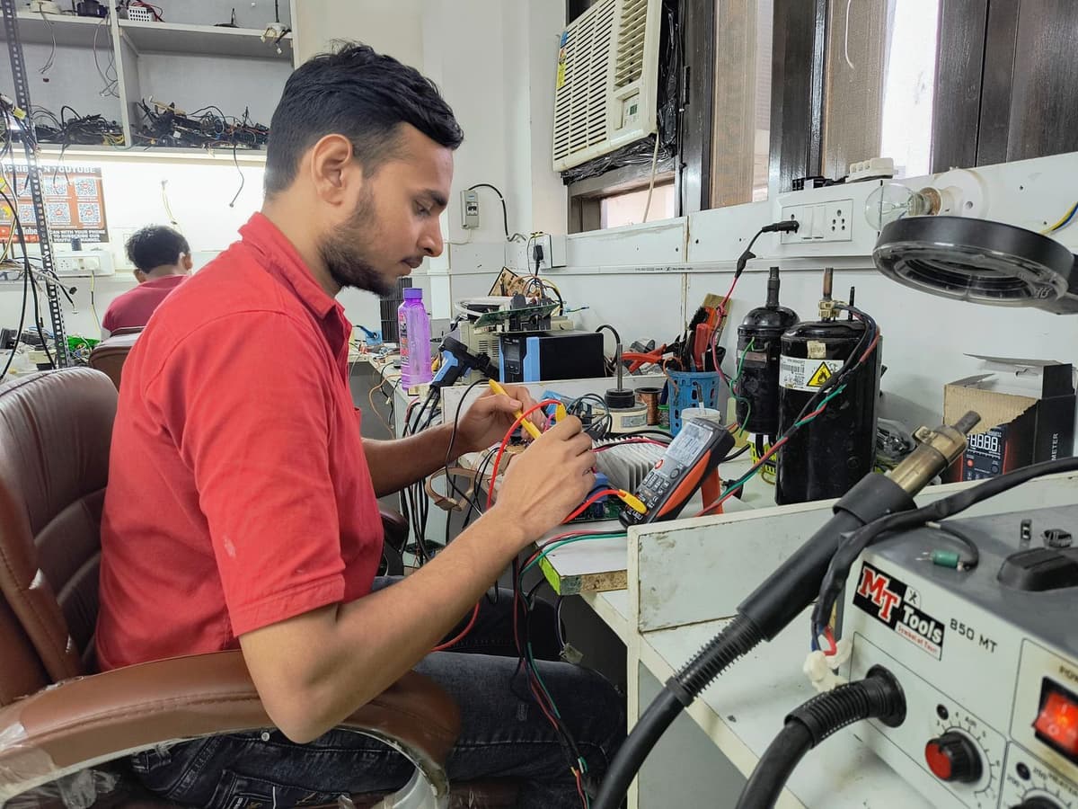 Técnico reparando la placa electrónica de un aire acondicionado con un multímetro en un taller