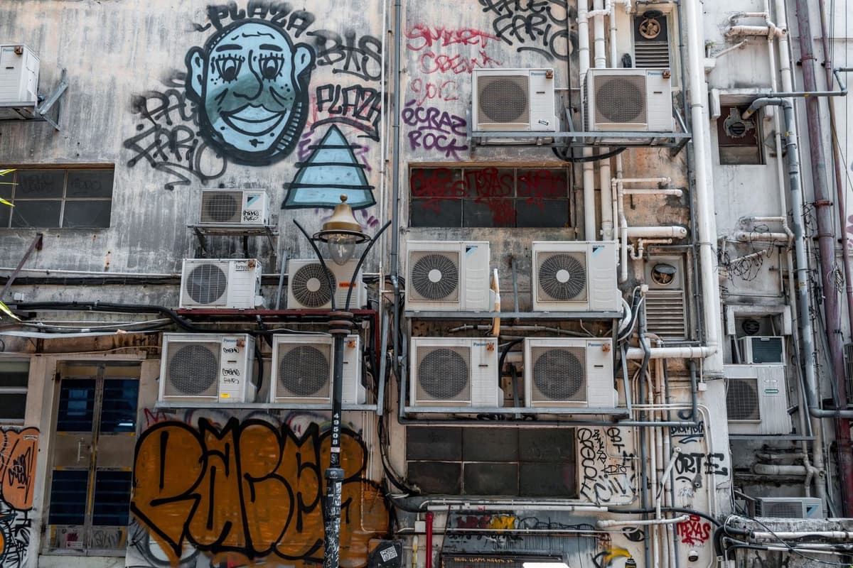 Talrijke buitenunits van airconditioners bevestigd aan een vervallen gevel vol graffiti
