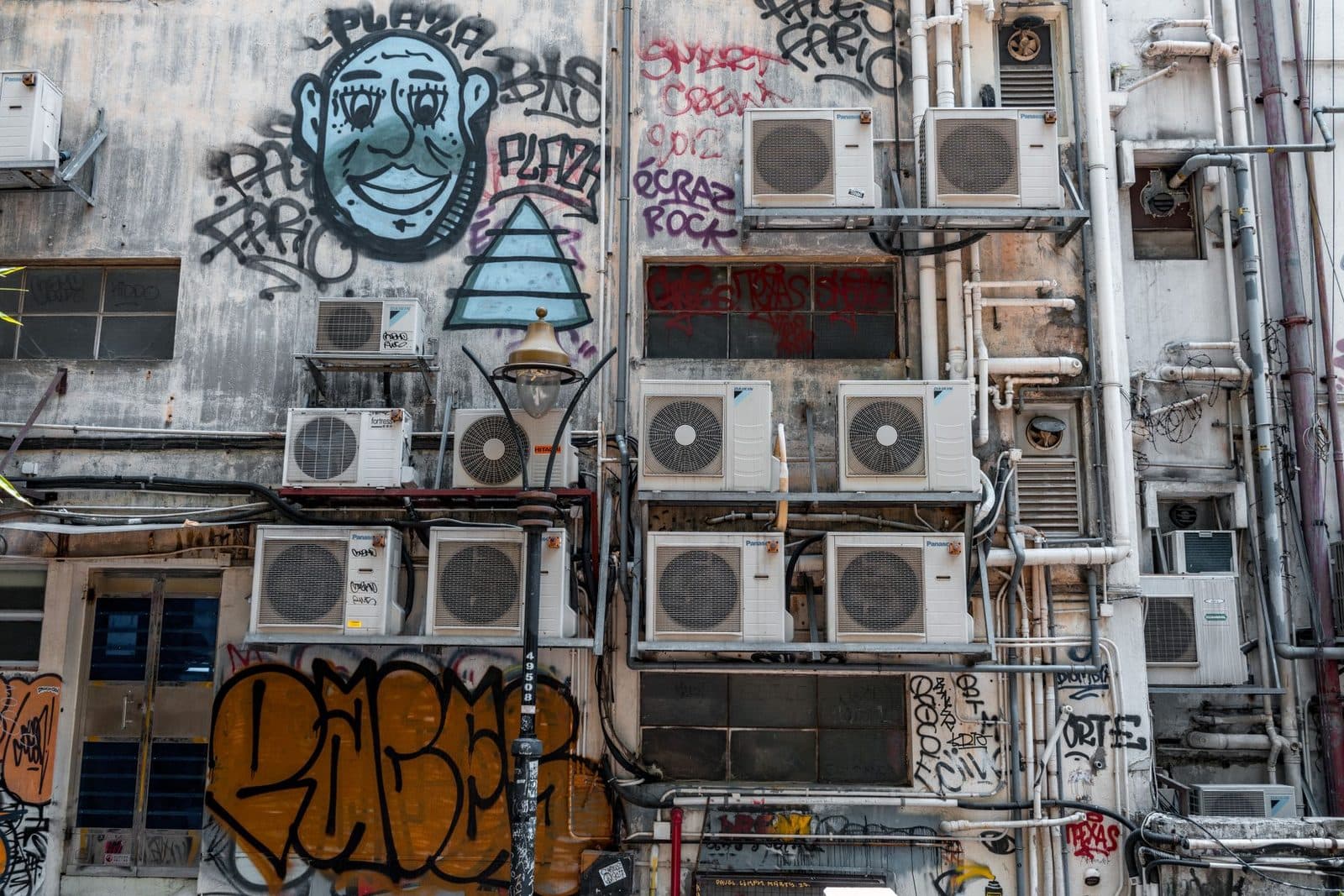 Nombreux groupes extérieurs de climatisation fixés sur une façade dégradée couverte de graffitis