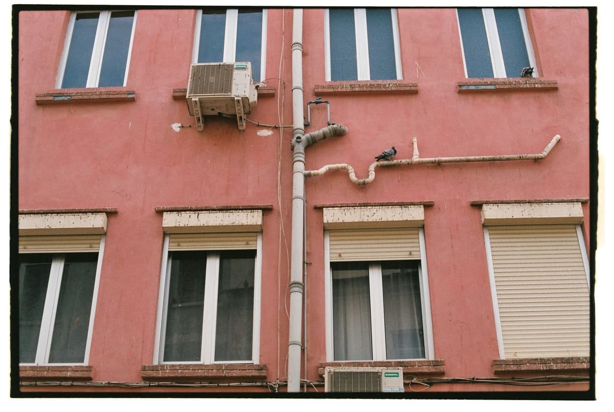Außeneinheiten von Klimaanlagen an der rosafarbenen Fassade eines Gebäudes mit Fenstern und Fensterläden
