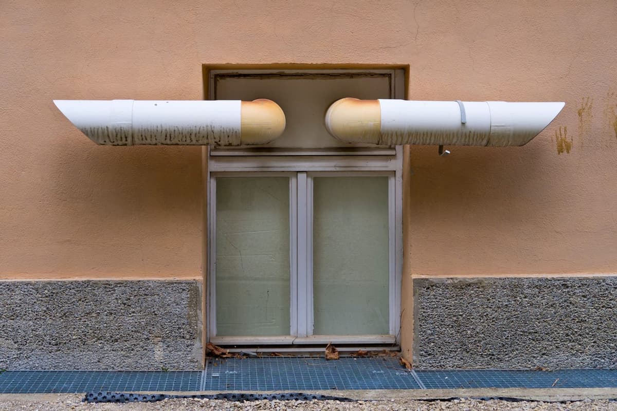 Deux conduits d'aération blancs et jaunes installés sur un mur beige au-dessus d'une fenêtre.