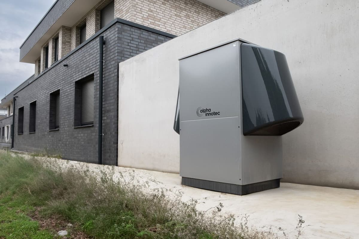 Unità esterna grigia di una pompa di calore aria-aria installata su una piastra lungo il muro di una casa