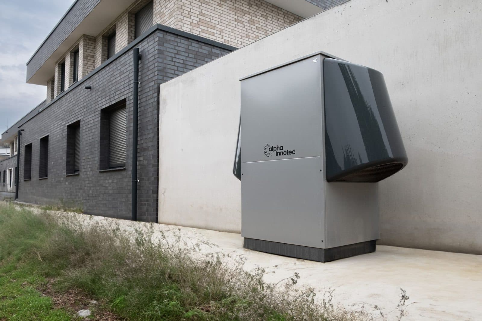 Unité extérieure grise d'une pompe à chaleur air-air installée sur une dalle le long d'un mur de maison