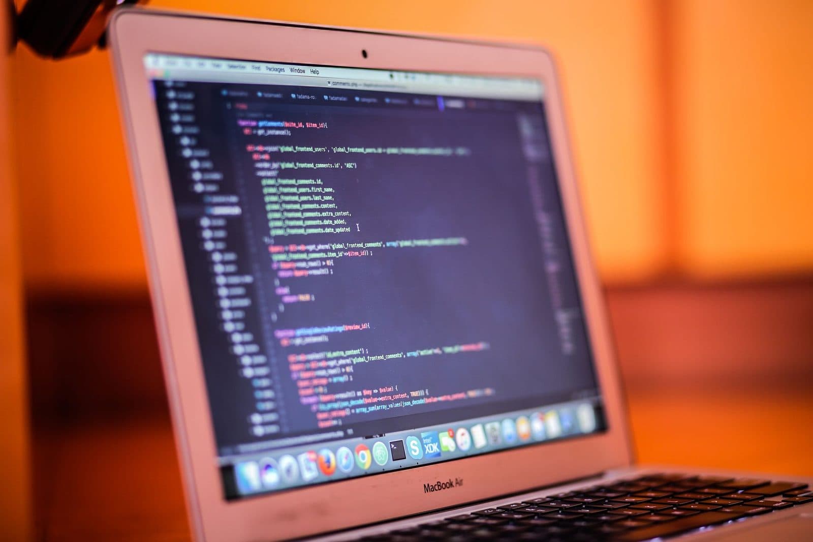 MacBook Air aperto con codice sorgente visualizzato sullo schermo, su sfondo arancione