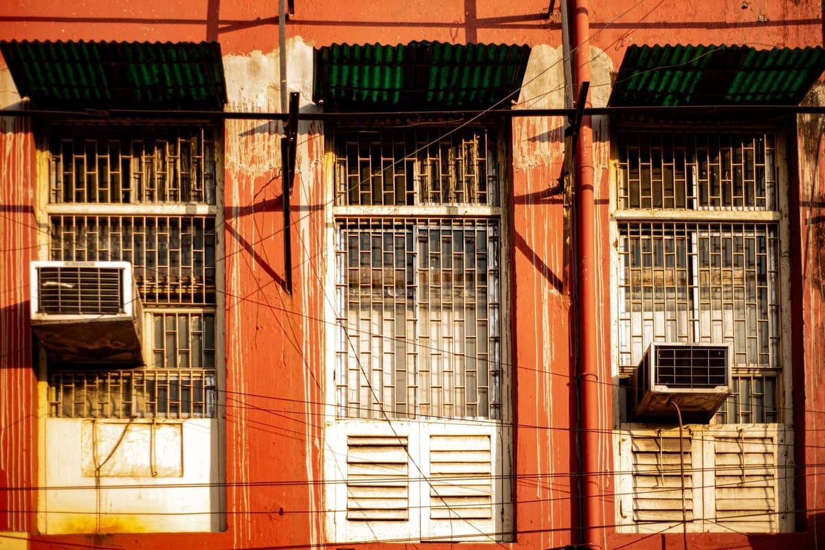 Aparelhos de ar condicionado de janela instalados na fachada vermelha de um edifício com janelas gradeadas