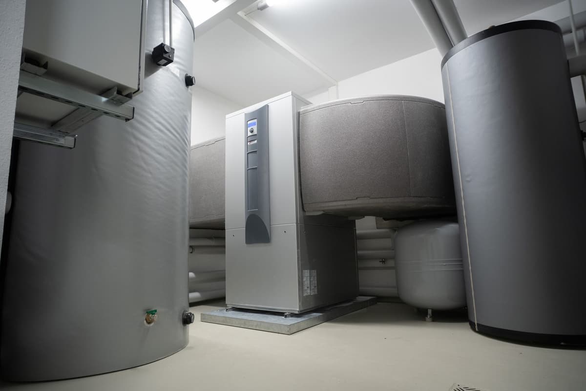 Technische Heizinstallation mit Warmwasser speichern und Wärmepumpeneinheit in einem weißen Raum.