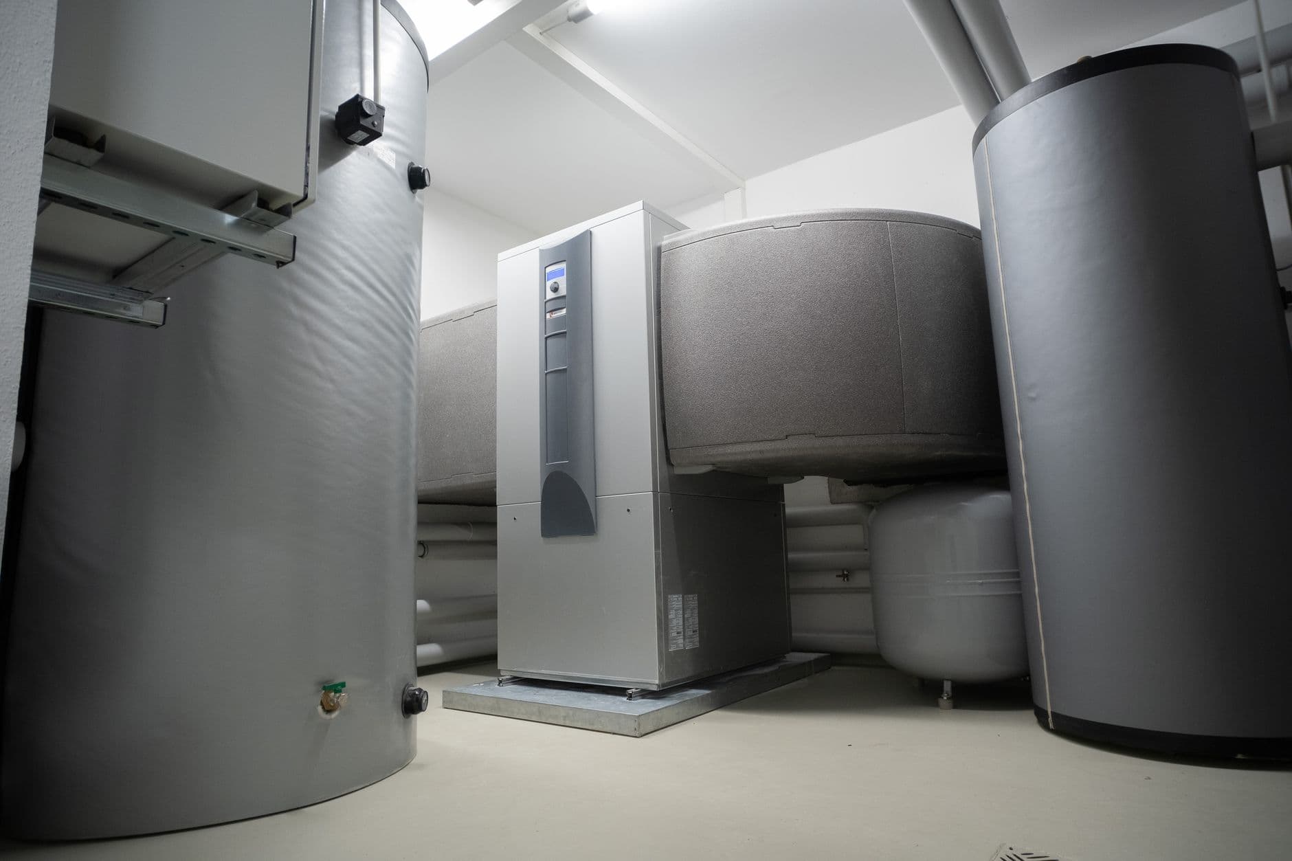 Installazione tecnica di riscaldamento con boiler per l'acqua calda e unità di pompa di calore in una stanza bianca.