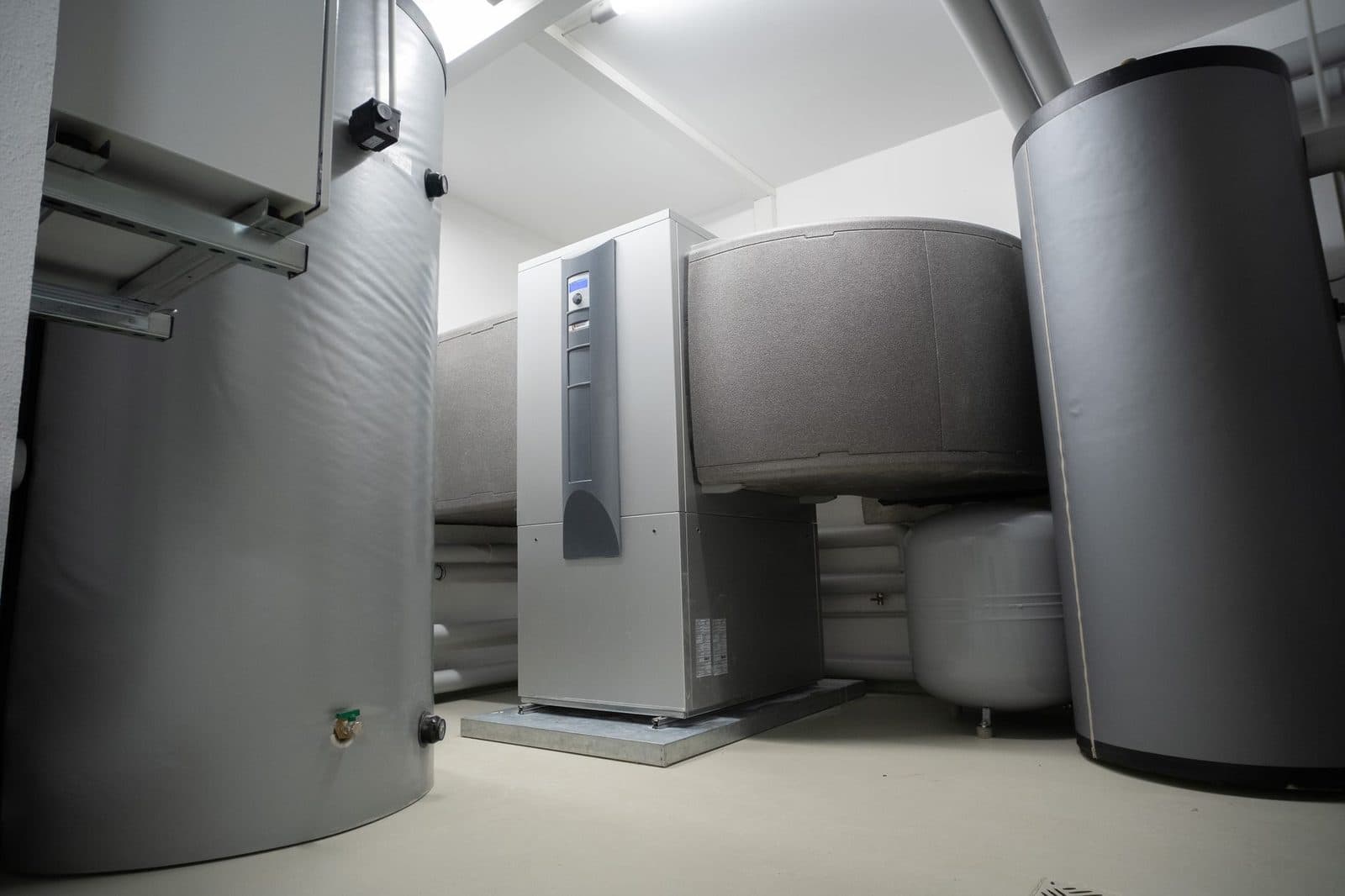 Technical installation including hot water tanks and a heat pump unit in a white room.
