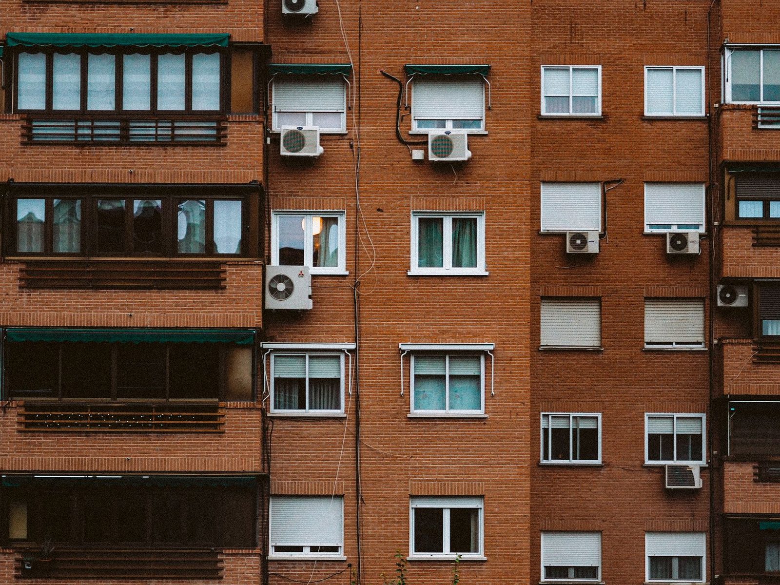 Fachada de ladrillo de un edificio de viviendas con numerosas unidades exteriores de aire acondicionado bajo las ventanas