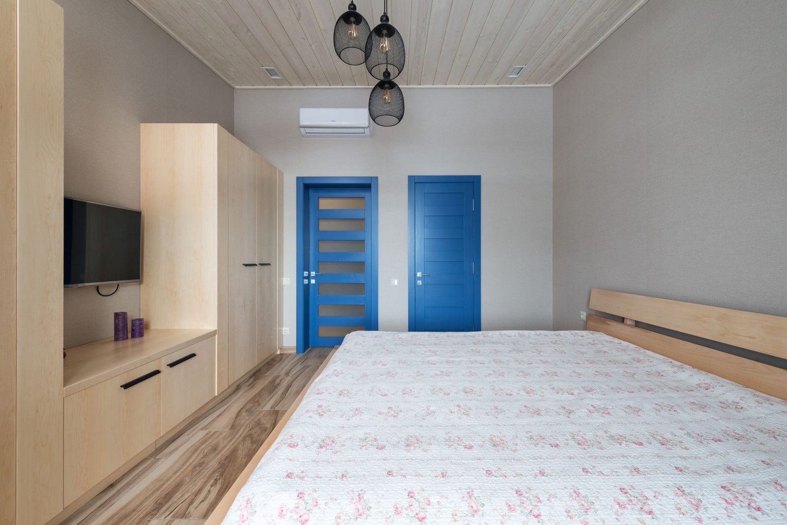 Climatizzatore a parete bianco installato in una camera con letto matrimoniale, porte blu e mobili in legno chiaro