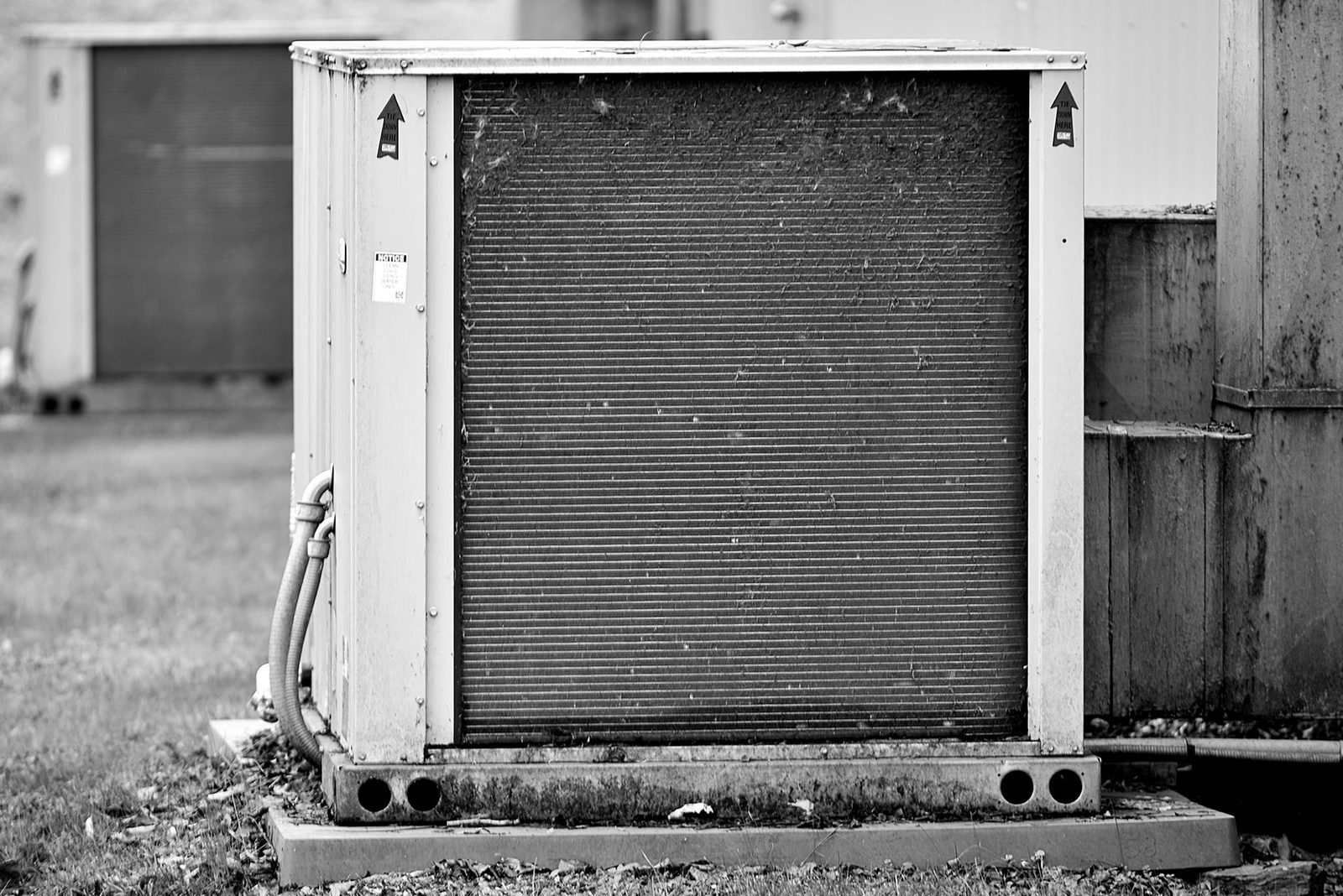 Unità esterna di climatizzazione posata su una platea in calcestruzzo lungo un edificio, foto in bianco e nero