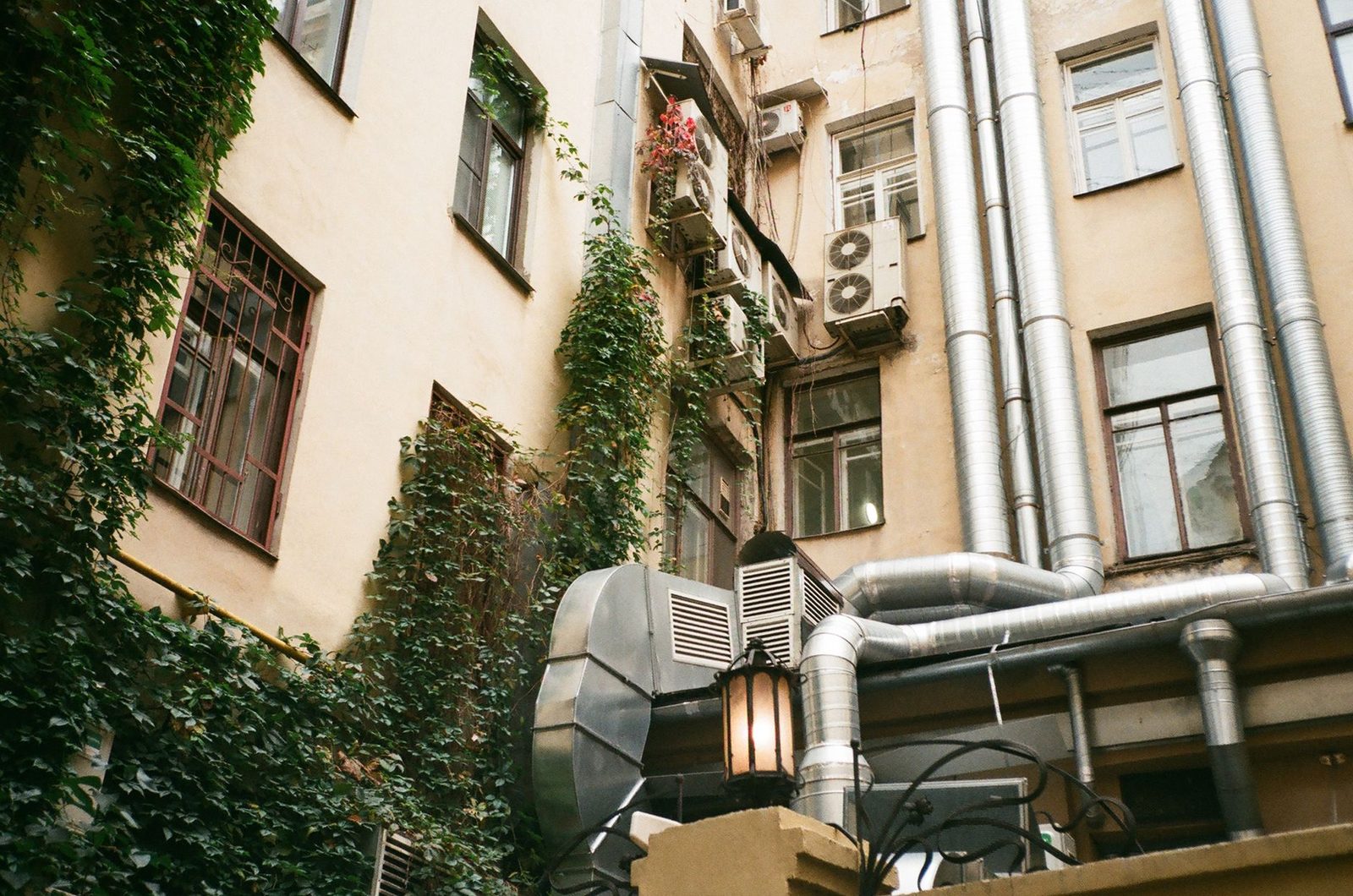 Unidades exteriores de aire acondicionado y conductos de ventilación en la fachada de un edificio antiguo cubierto de hiedra