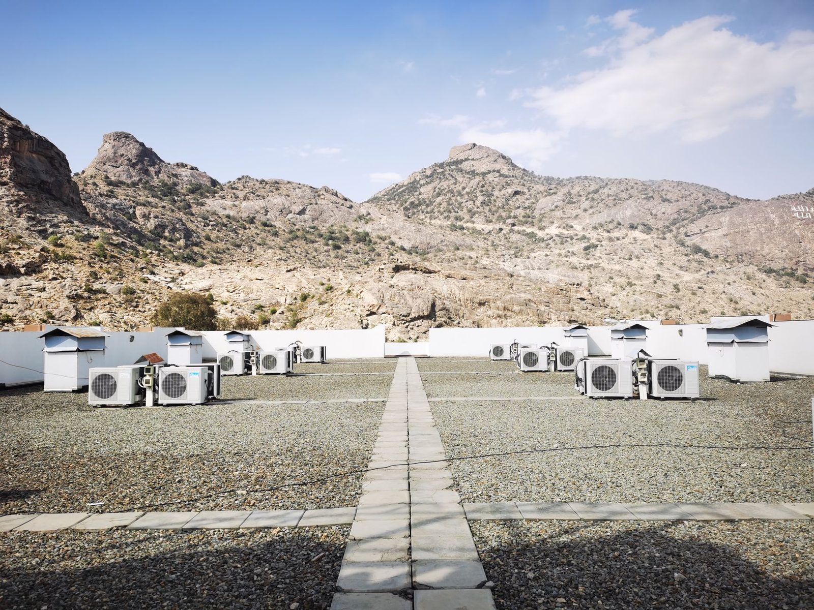 Air conditioner outdoor units lined up on a gravel roof, in front of an arid mountain landscape