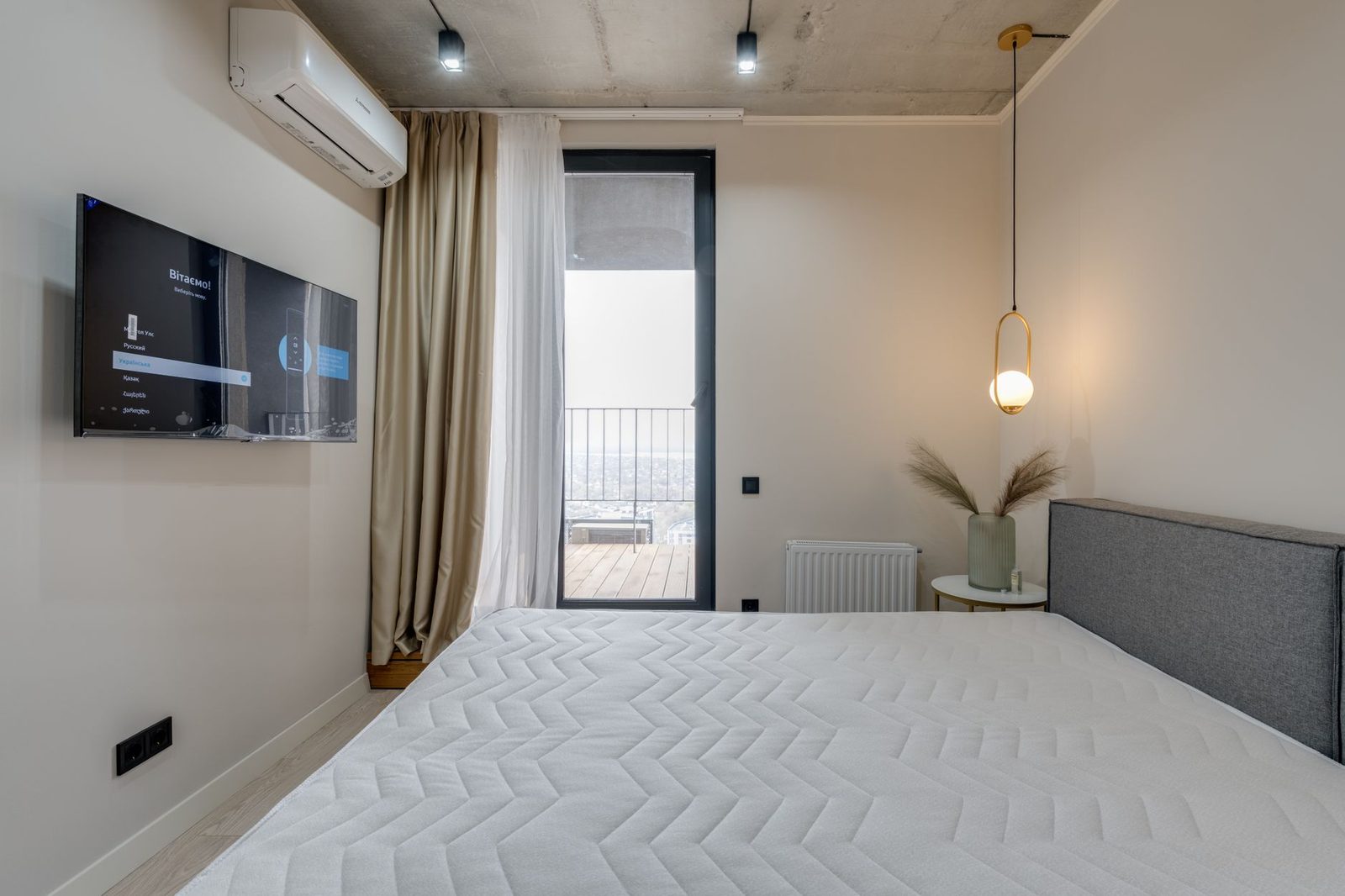 Weißes reversibles Wandklimagerät über einem Fernseher in einem Schlafzimmer mit Bett und Fensterfront