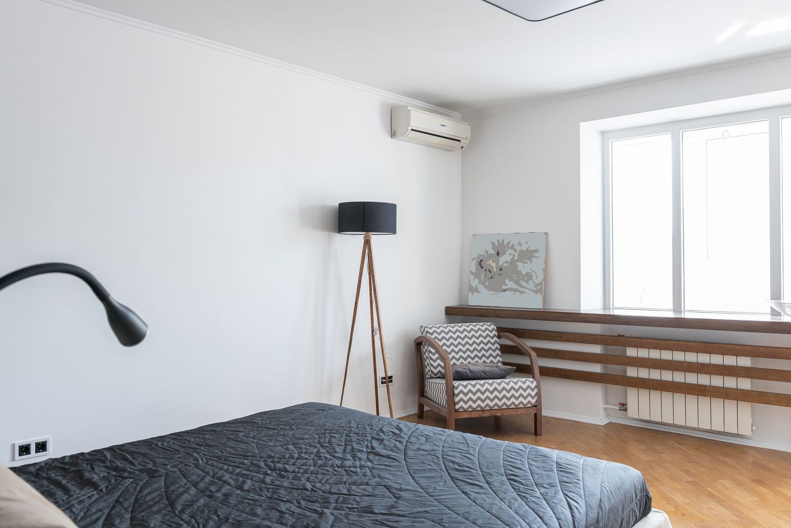 Weißes Wandklimagerät in einem hellen Schlafzimmer mit Bett, Stehlampe und Sessel