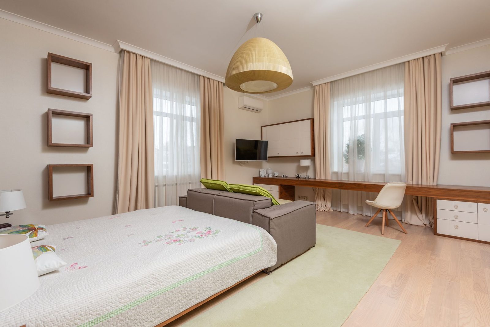 Helles Schlafzimmer mit Wandgerät einer reversiblen Klimaanlage über dem Fernseher, Bett und Holzschreibtisch