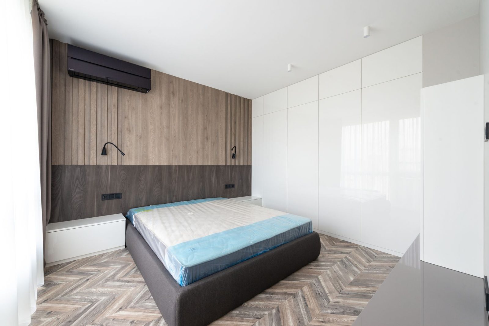 Unidade mural de ar condicionado reversível instalada num quarto moderno com cama e armários brancos