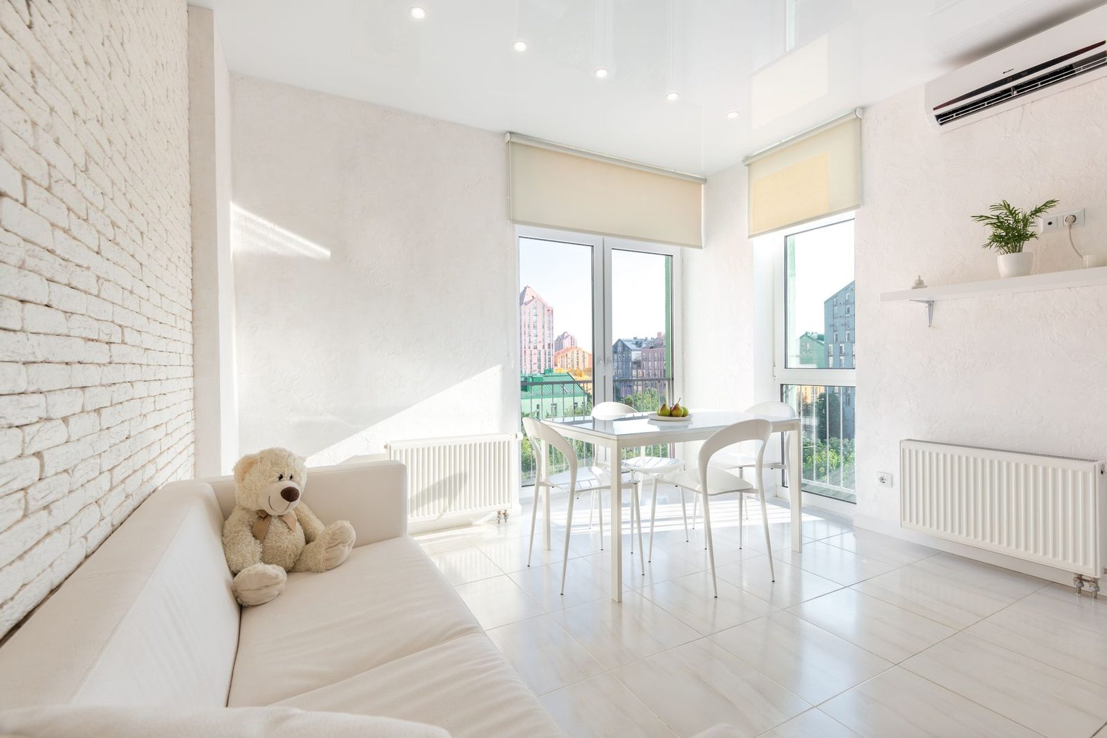 Split de aire acondicionado con bomba de calor fijado a la pared de un salón luminoso con sofá, mesa y radiadores