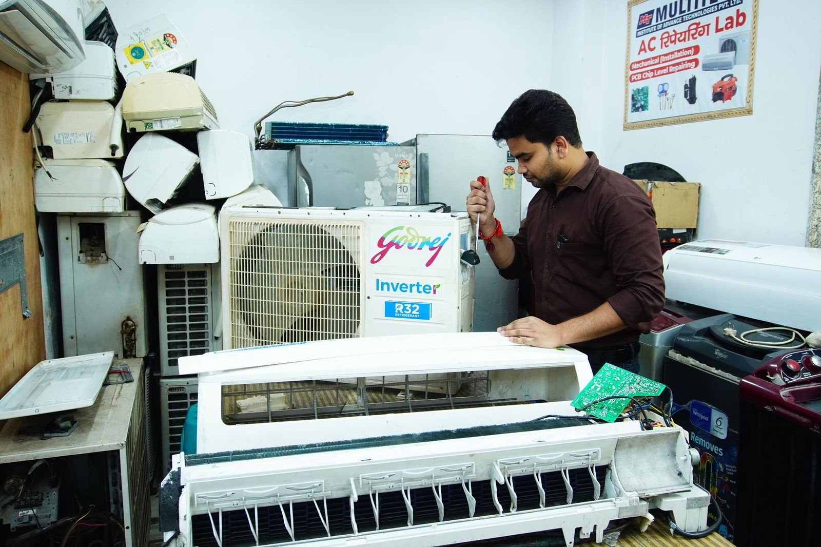 Tecnico che smonta un'unità interna di climatizzatore in un'officina di riparazione, cacciavite in mano