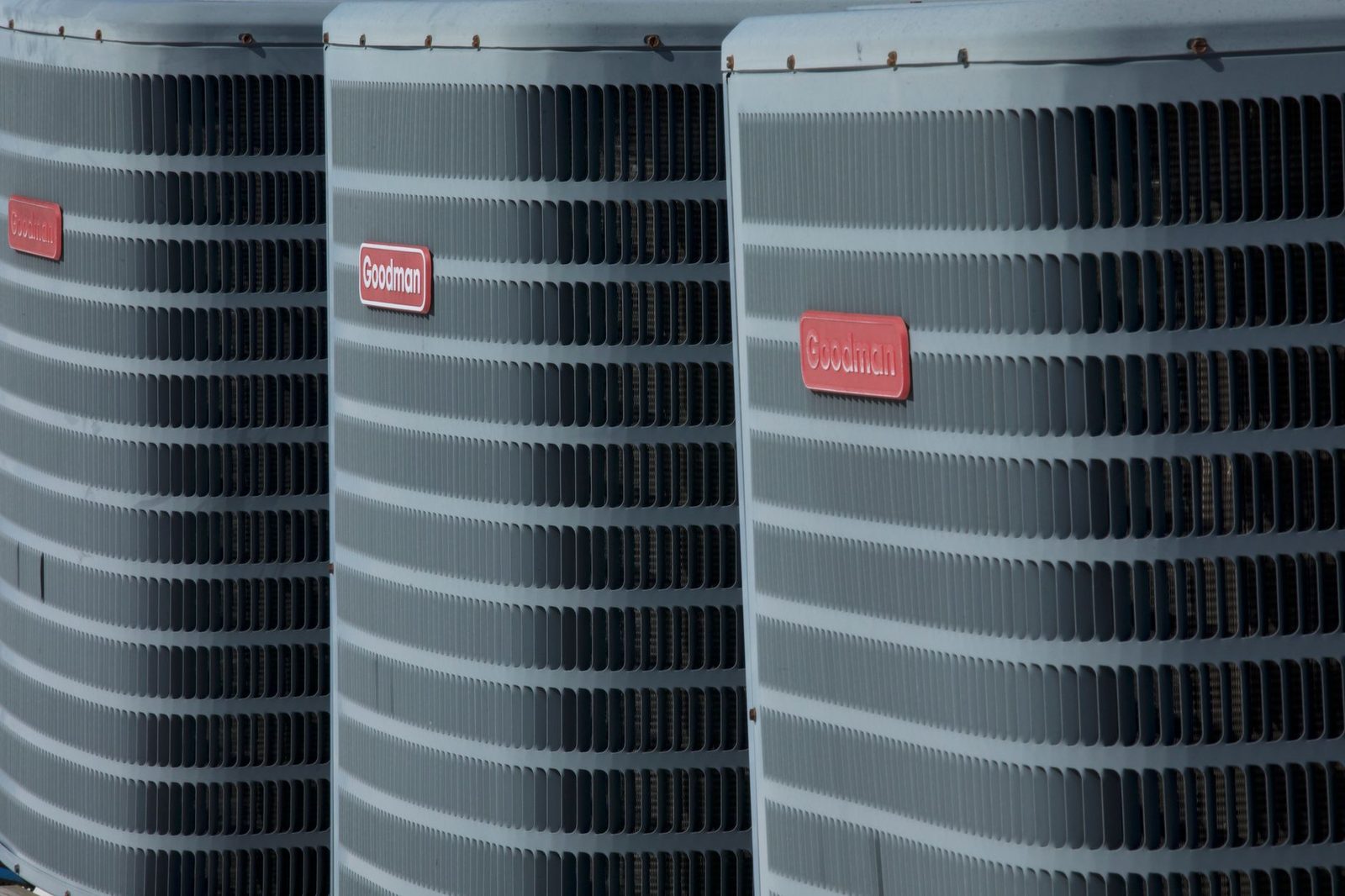 Drie buitenunits van airconditioning op een rij, grijze metalen roosters en rode merkplaatjes