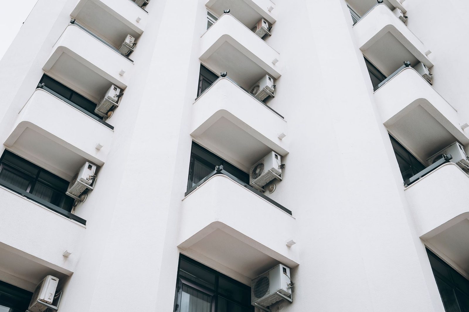 Unités extérieures de climatisation fixées sous les balcons d'un immeuble blanc, vue en contre-plongée
