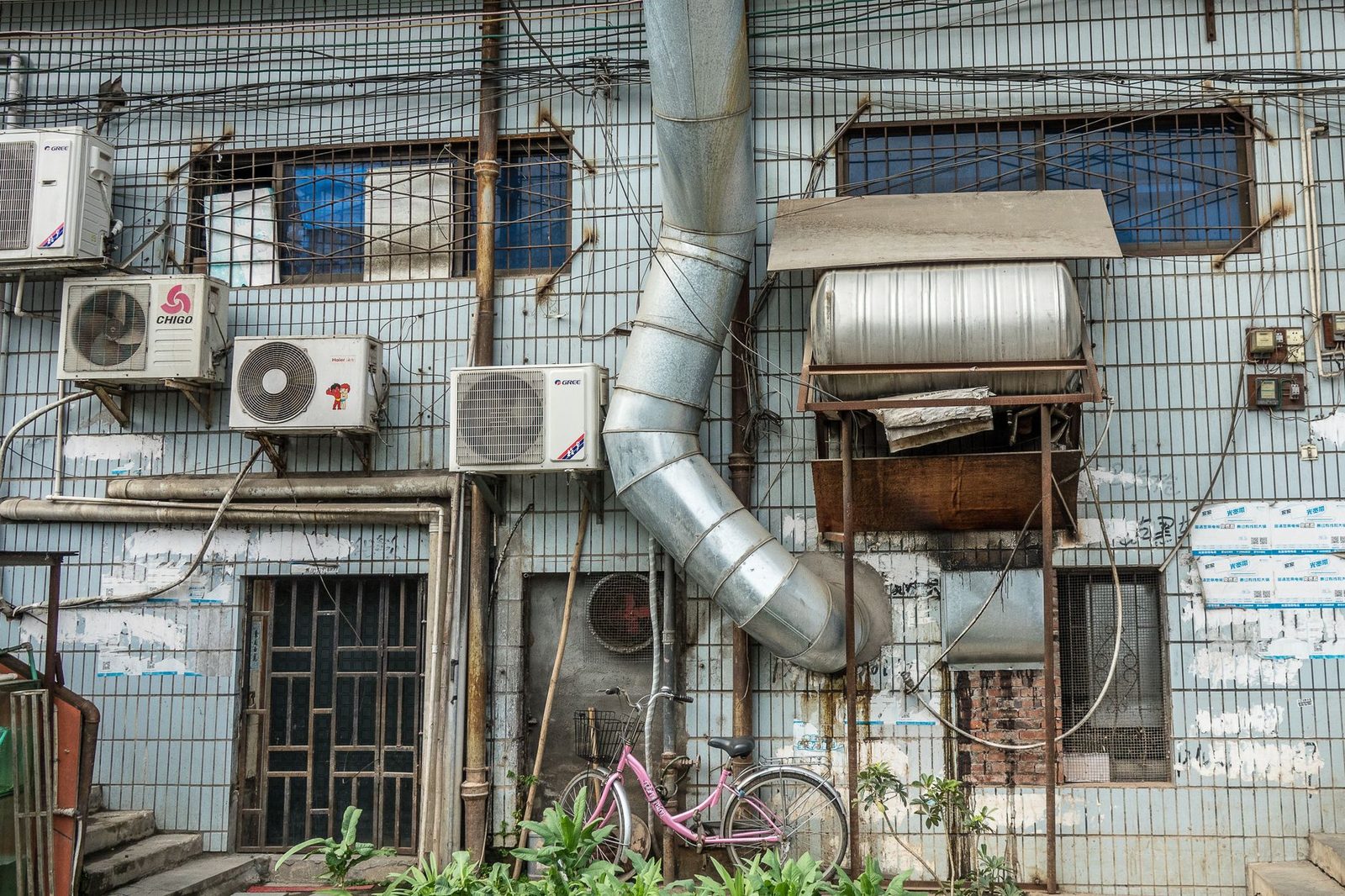 Buitenunits van airconditioners bevestigd aan een betegelde muur met kabels, metalen kanaal en een fiets