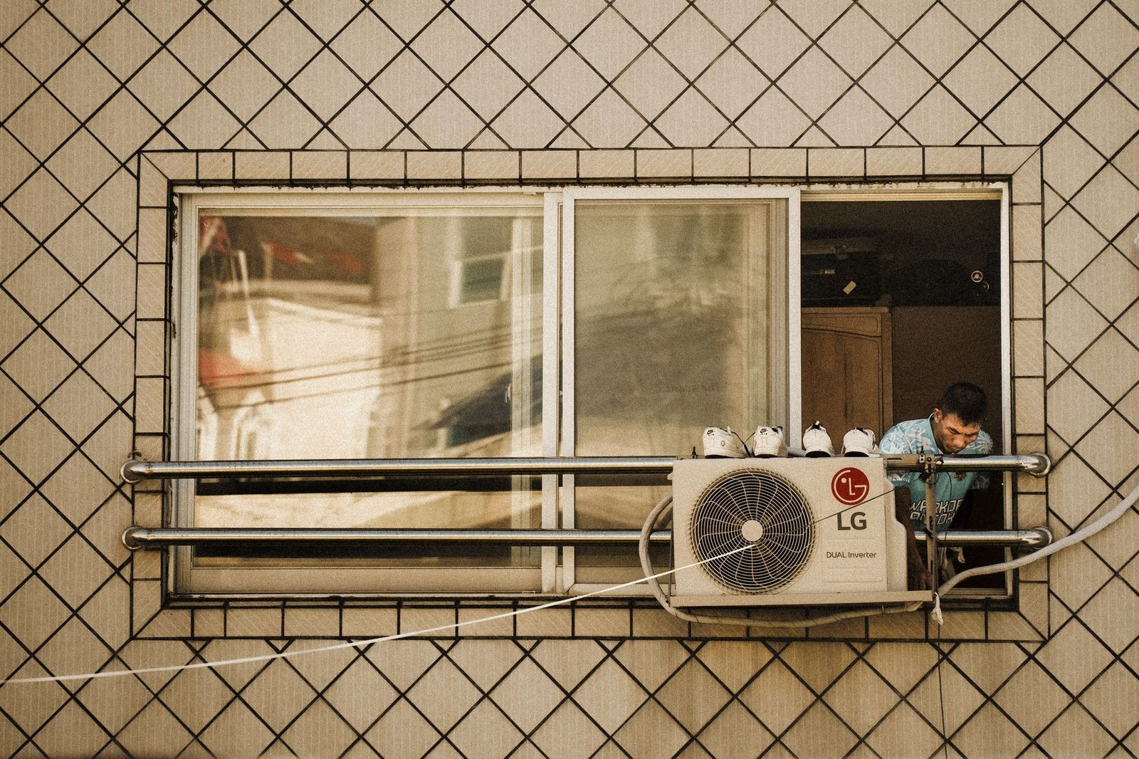 Buitenunit van een airconditioning bevestigd onder een raam, met daarboven een man die uit het raam leunt