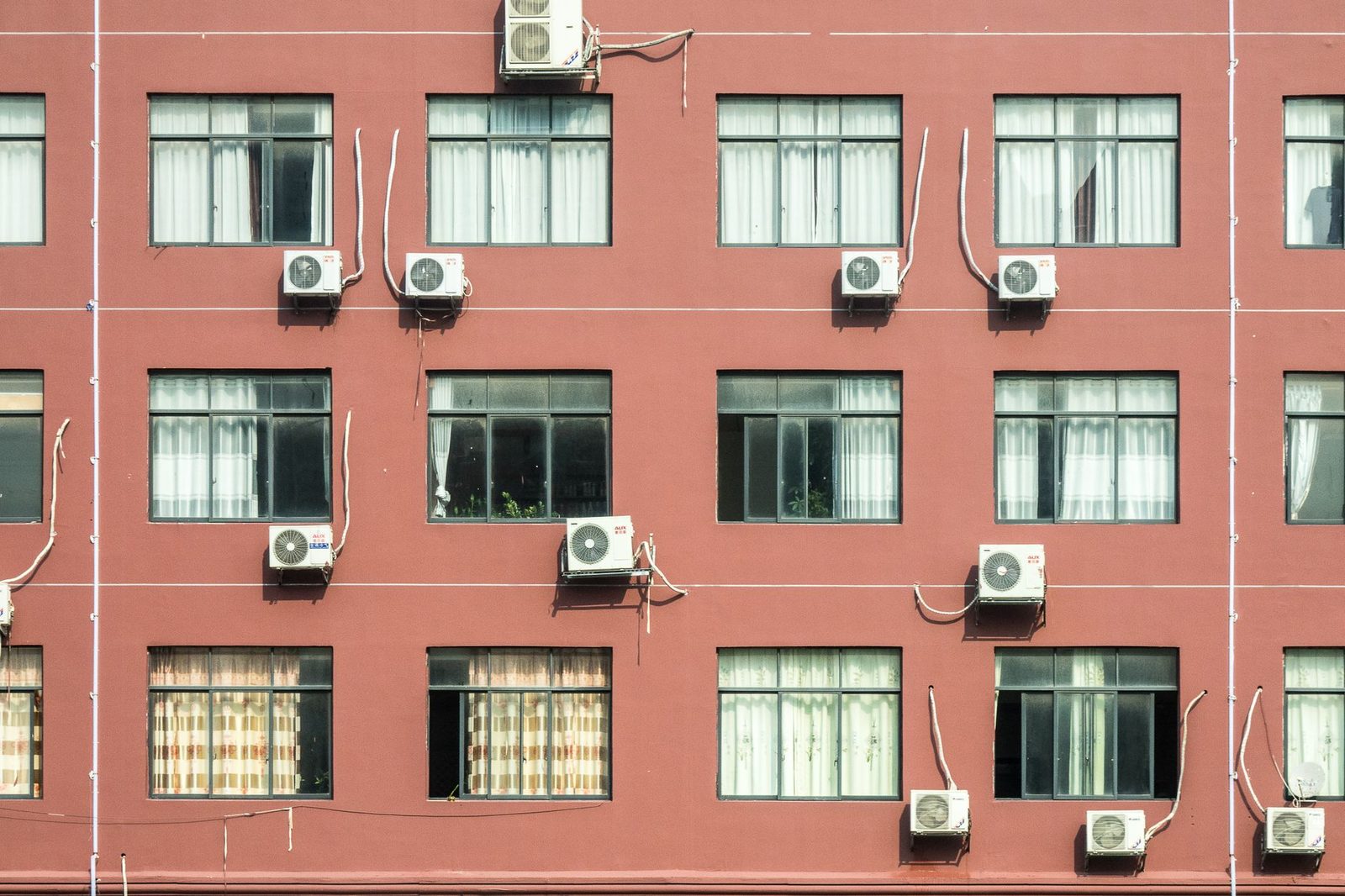 Unités extérieures de climatiseurs fixées sous les fenêtres d'une façade d'immeuble rouge