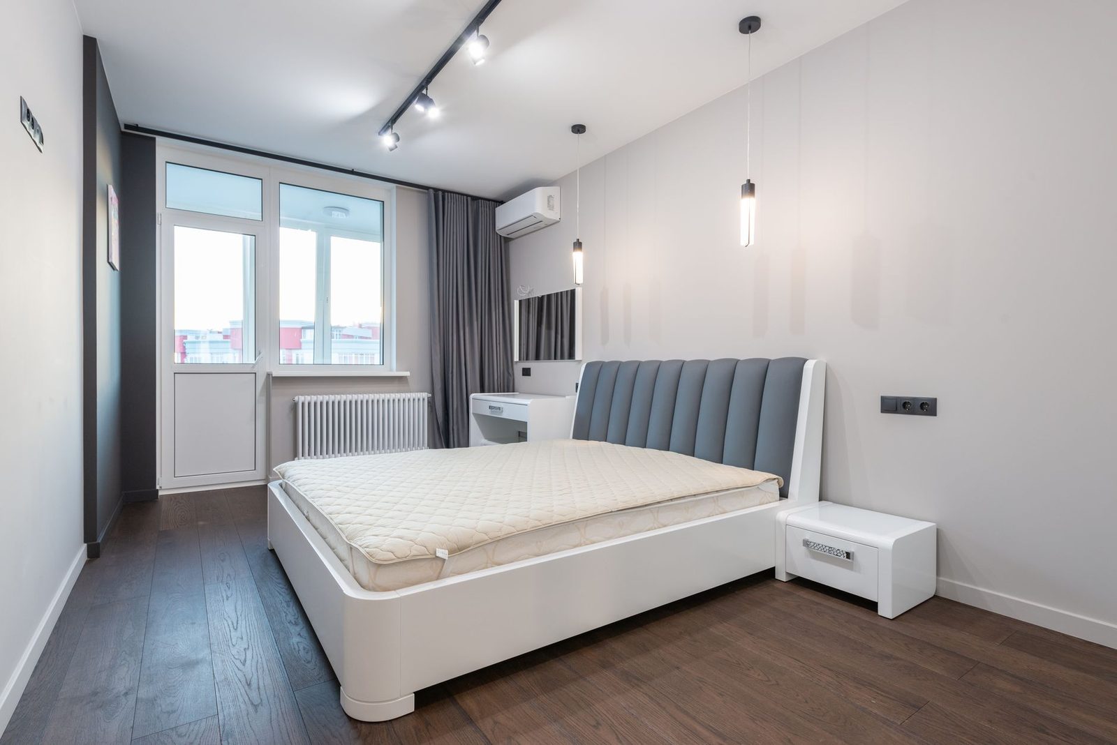 Dormitorio moderno con unidad mural de aire acondicionado reversible sobre la cama y radiador bajo la ventana