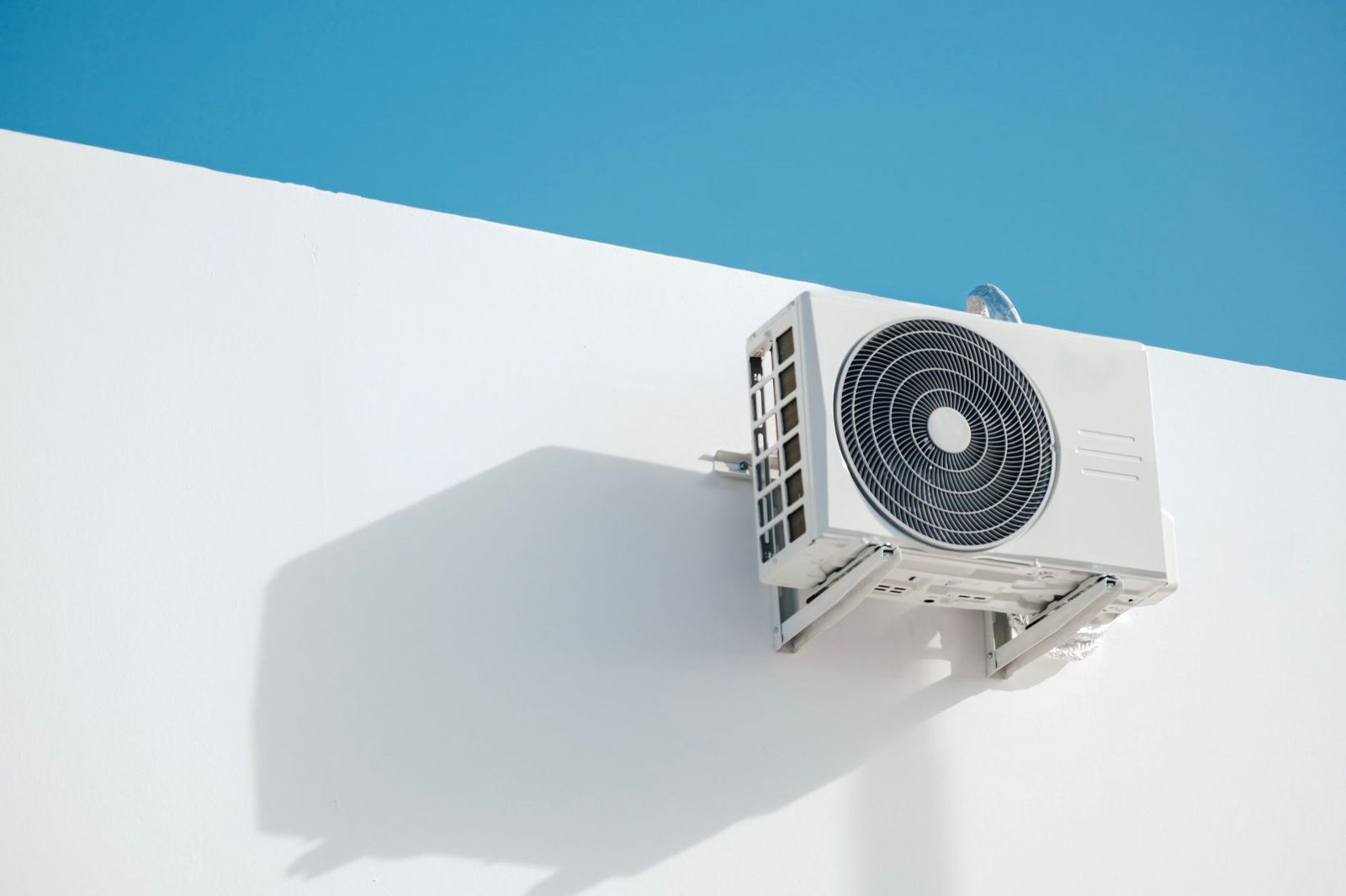 White outdoor air conditioning unit fixed to a white wall under a blue sky