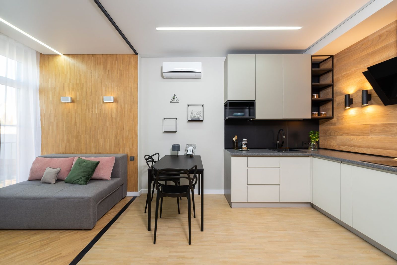 Climatizzatore a parete bianco installato in un soggiorno moderno con cucina a vista, tavolo e divano grigio