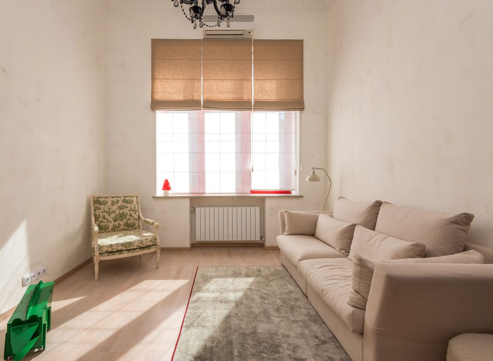Wandunit van een airconditioning boven een raam in een lichte woonkamer met beige bank en fauteuil