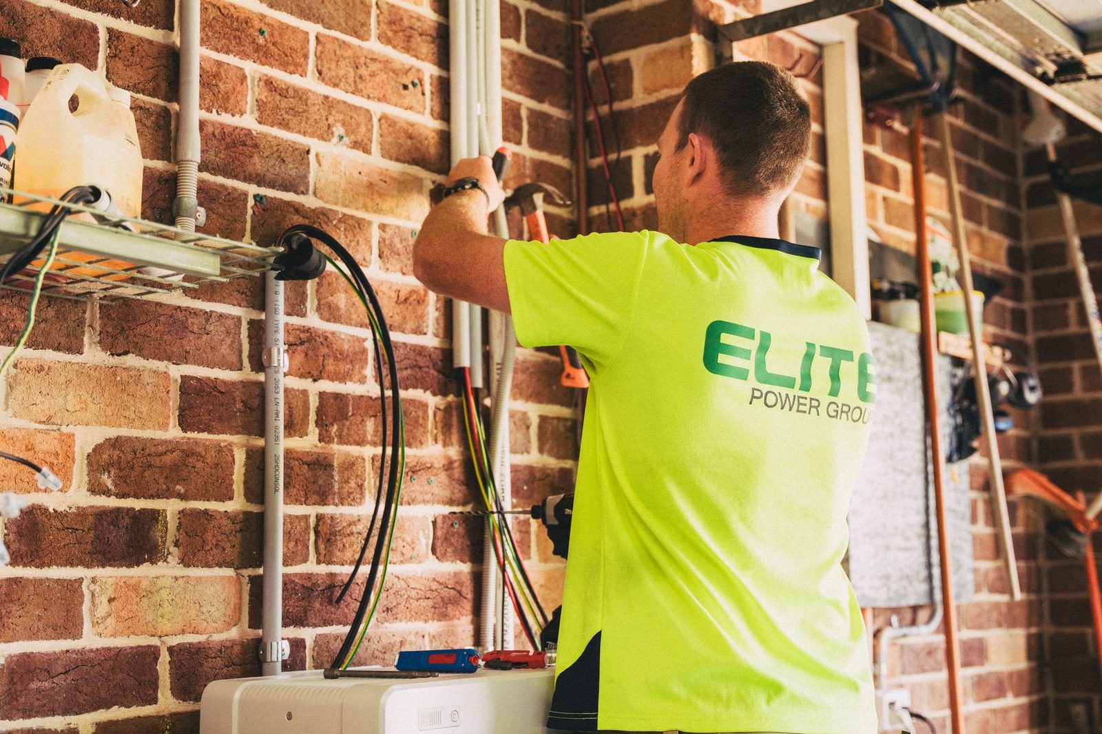Technicus in fluorgeel T-shirt die leidingen en elektriciteitskabels op een bakstenen muur installeert
