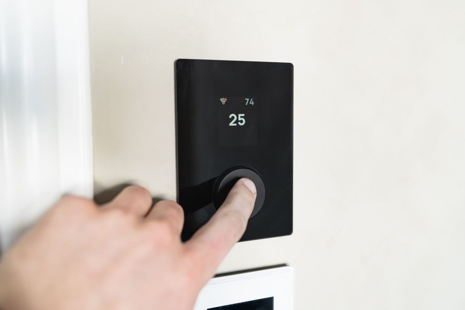 Hand die een zwarte wandthermostaat met 25 graden instelt in een lichte kamer