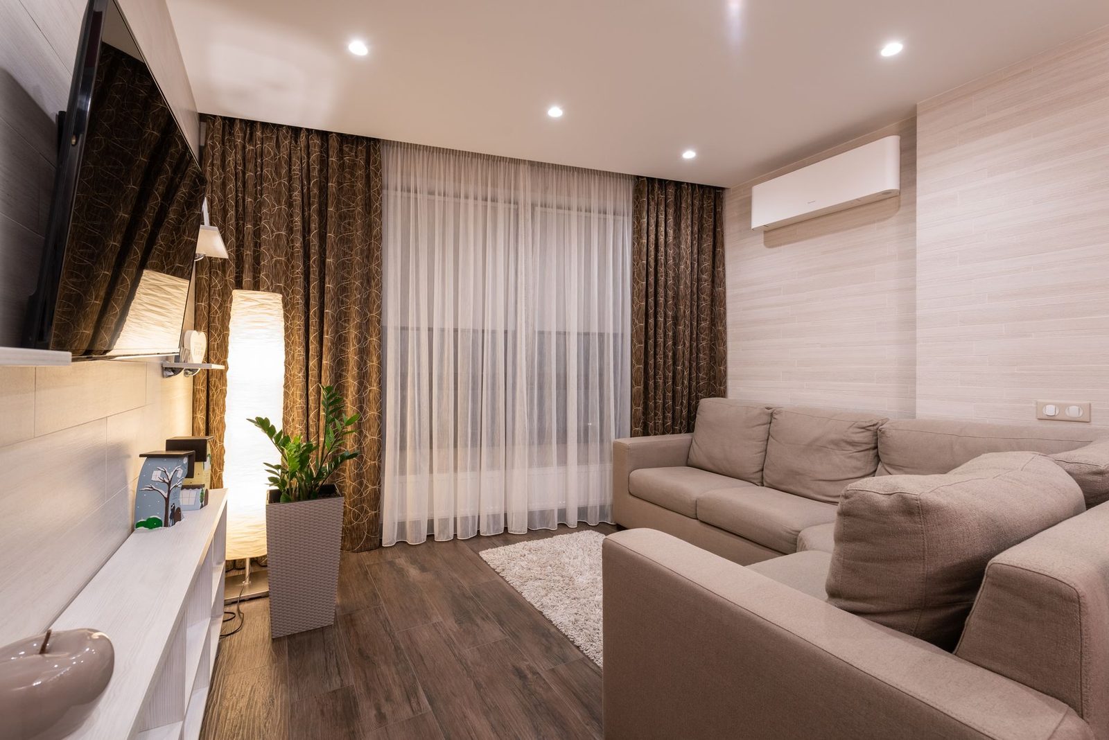 Climatiseur réversible mural blanc installé dans un salon moderne avec canapé beige et parquet