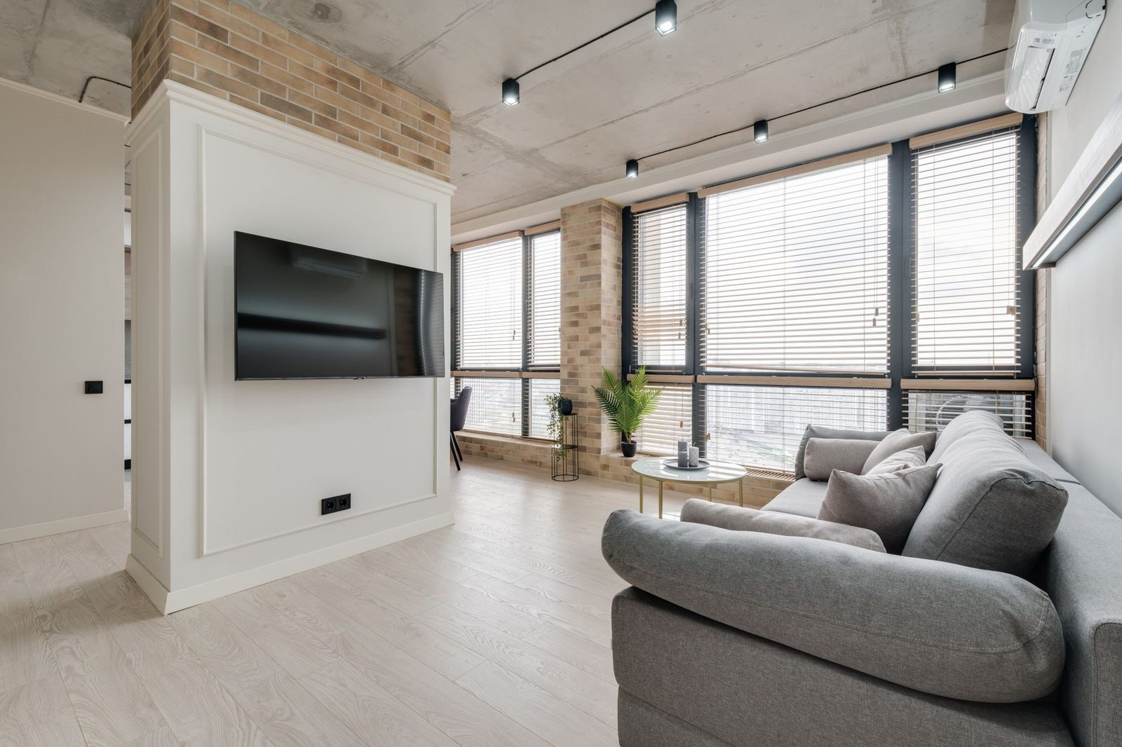 Climatiseur réversible mural blanc installé en hauteur dans un salon lumineux avec canapé gris