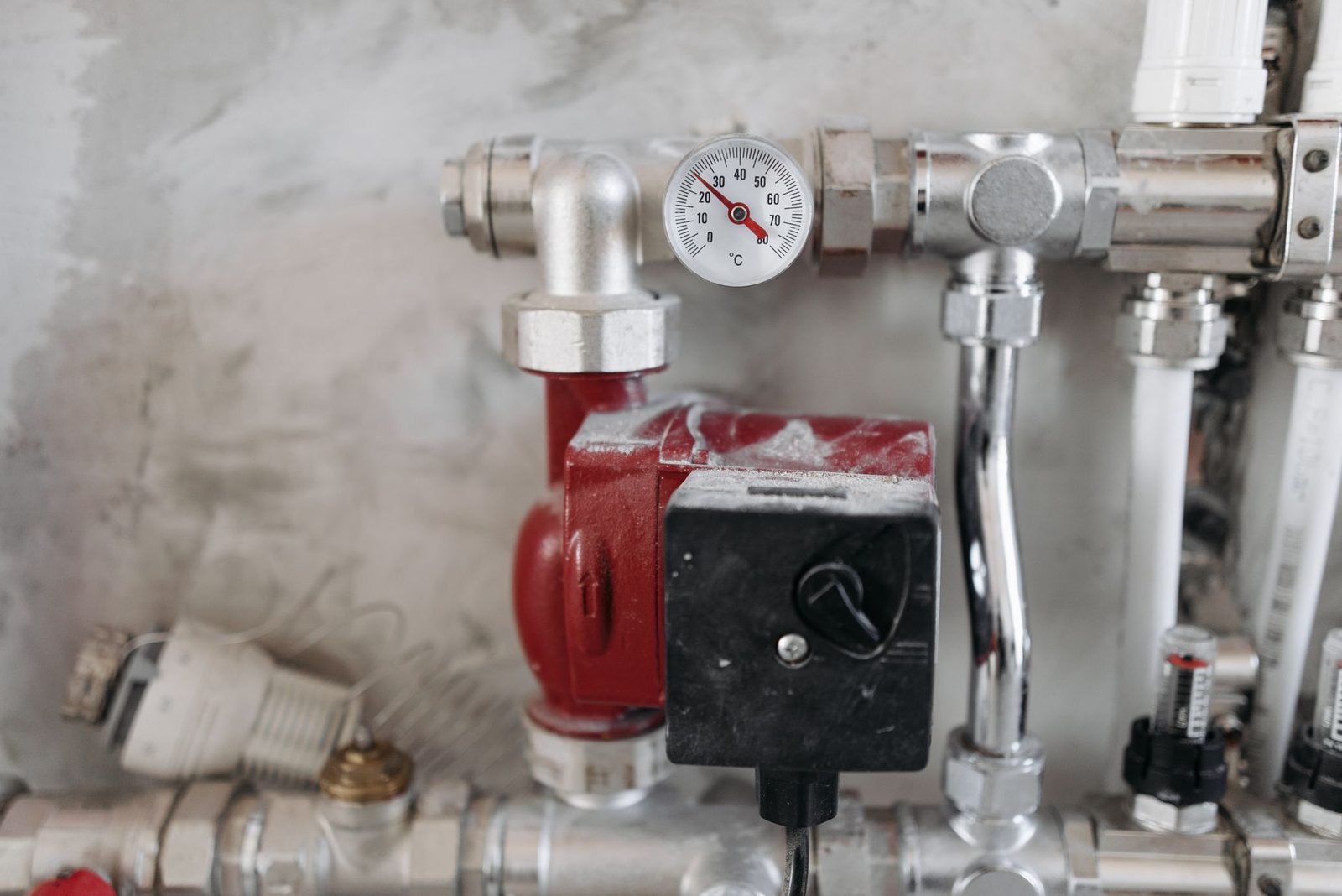 Rode circulatiepomp, thermometer en verchroomde leidingen van een cv-installatie in huis