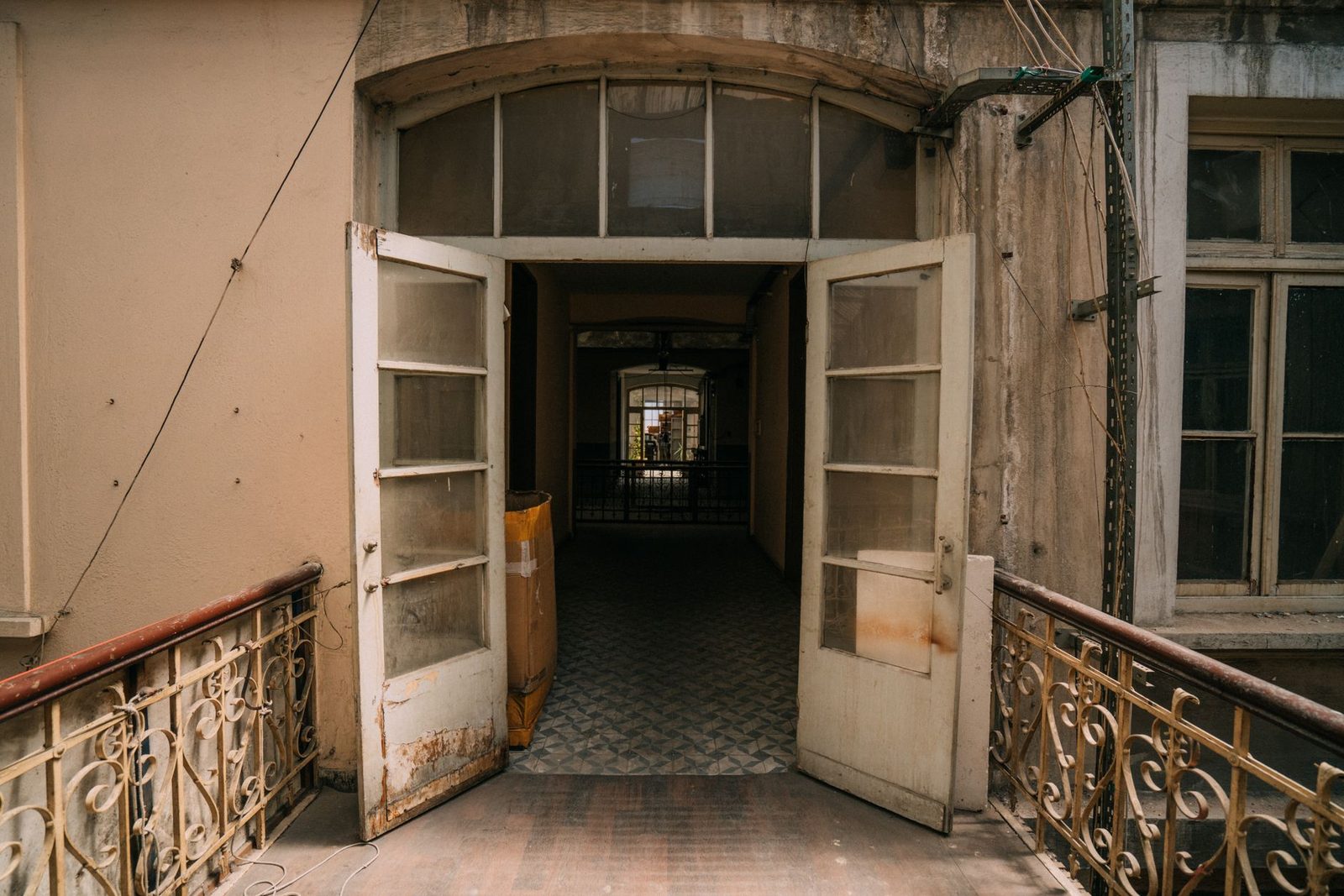 Porta a vetri in legno aperta su un corridoio piastrellato di un vecchio palazzo, ringhiere in ferro battuto